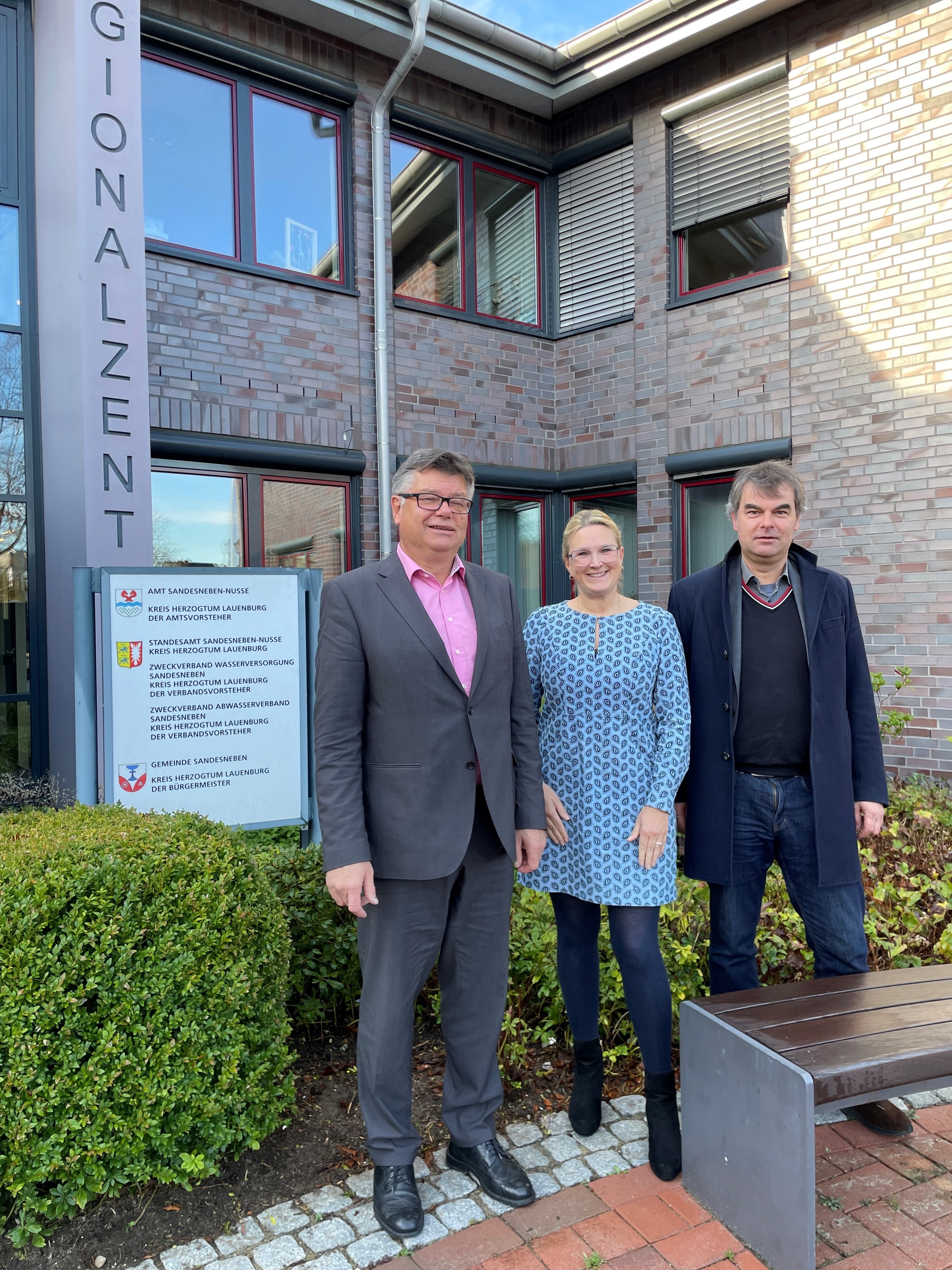 Im Bild zu sehen sind von links nach rechts, der Amtsvorsteher Ulrich Hardtke, die leitende Verwaltungsbeamtin Tina Knuth und der Landtagsabgeordnete  Oliver Brandt vor dem Regionalzentrum in Sandesneben.