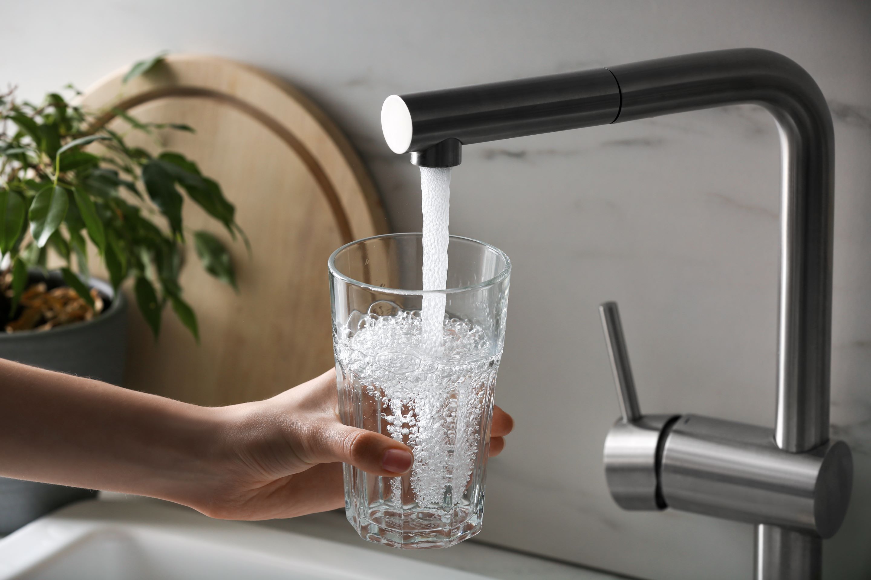 Hand hält ein Glas unter einen Wasserhahn, aus dem frisches Leitungswasser läuft.