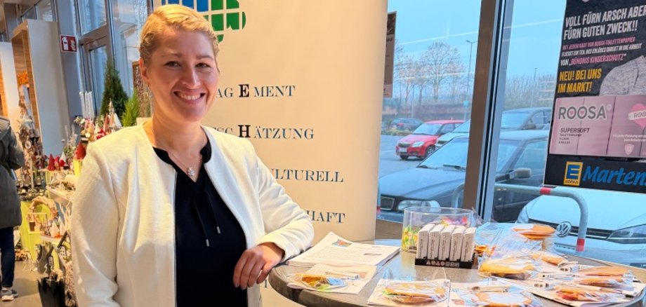 Eine Mitarbeiterin des Amtes Sandesneben-Nusse steht lächelnd neben einem Roll-Up-Banner und einem Stehtisch mit Informationsmaterial in einem Eingangsbereich.