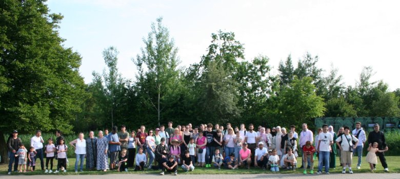 Großes Gruppenfoto von rund 100 Personen – darunter Kinder, Jugendliche und Erwachsene – die gemeinsam vor einer Baumkulisse im Serengeti-Park stehen. Die Gruppe besteht aus Geflüchteten und Ehrenamtlichen, die fröhlich in die Kamera blicken. Einige sitzen oder knien vorne, die meisten stehen nebeneinander auf dem Rasen. Der sonnige Tag und die entspannte Atmosphäre spiegeln sich in der offenen und herzlichen Stimmung wider.