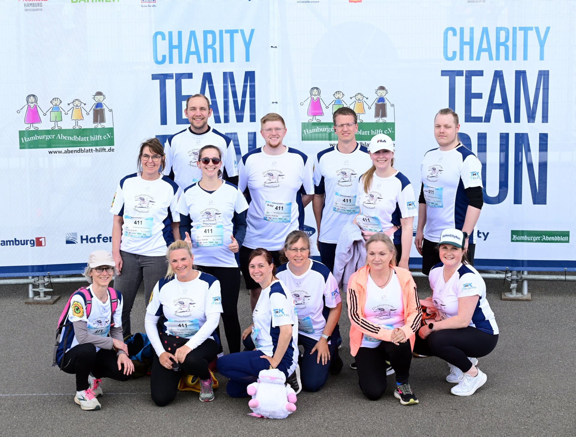 Das Laufteam „Die galoppierenden Amtsschimmel“ des Amtes Sandesneben-Nusse posiert vor dem Banner des HafenCityRun 2025 in Hamburg.
