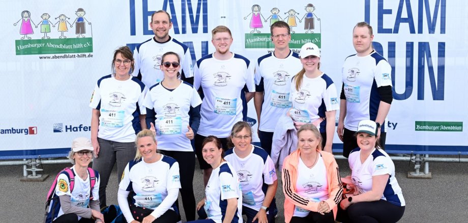 Das Laufteam „Die galoppierenden Amtsschimmel“ des Amtes Sandesneben-Nusse posiert vor dem Banner des HafenCityRun 2025 in Hamburg.