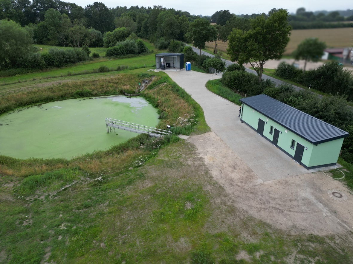 Klärteichanlage Grinau mit Teichbecken im Vordergrund und modernisiertem Betriebsgebäude im Hintergrund.