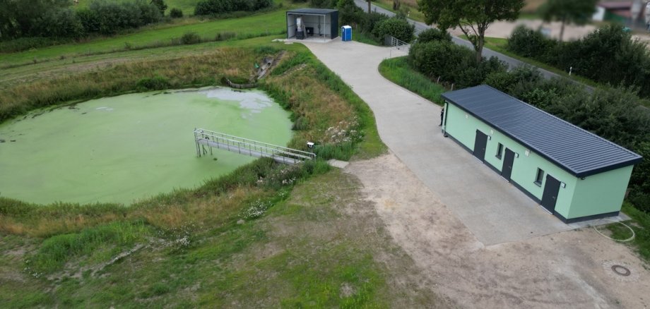Klärteichanlage Grinau mit Teichbecken im Vordergrund und modernisiertem Betriebsgebäude im Hintergrund.