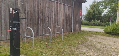 Fahrradreparaturstation an Holzgebäude Fahrradreparaturstation mit Werkzeugen und Luftpumpe neben einem Holzgebäude mit Fahrradständern.