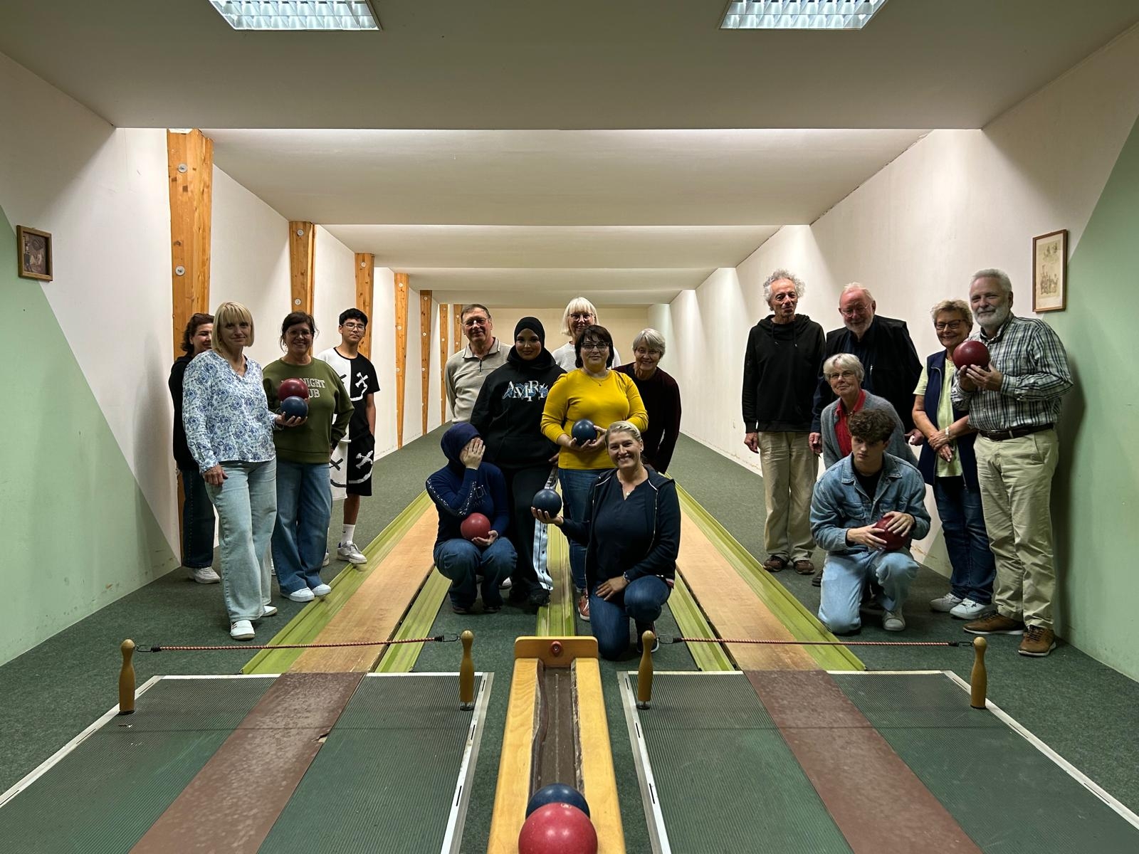 Gruppe von Männern und Frauen steht und kniet gemeinsam auf einer Kegelbahn für ein Gruppenfoto.