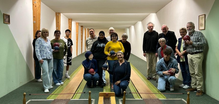 Gruppe von Männern und Frauen steht und kniet gemeinsam auf einer Kegelbahn für ein Gruppenfoto.