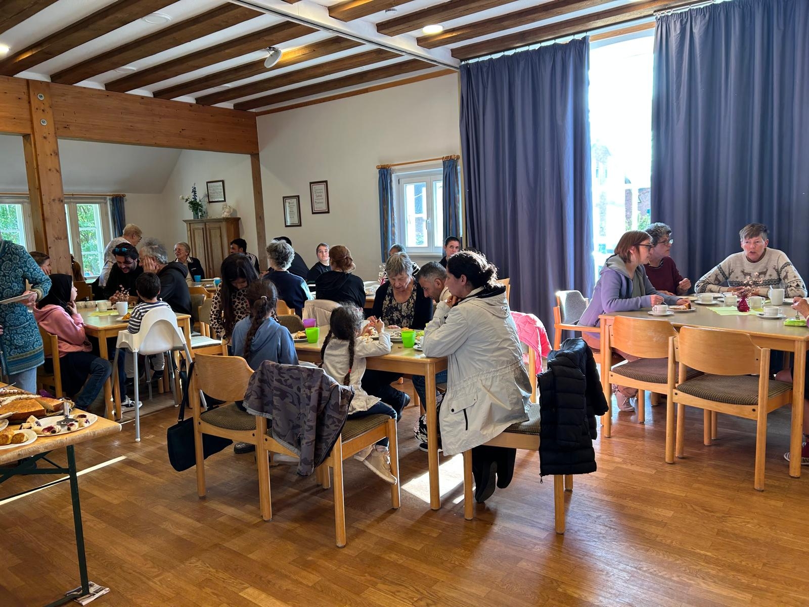 Gäste sitzen in Gruppen an Tischen und unterhalten sich beim gemeinsamen Kaffeetrinken in gemütlicher Atmosphäre.