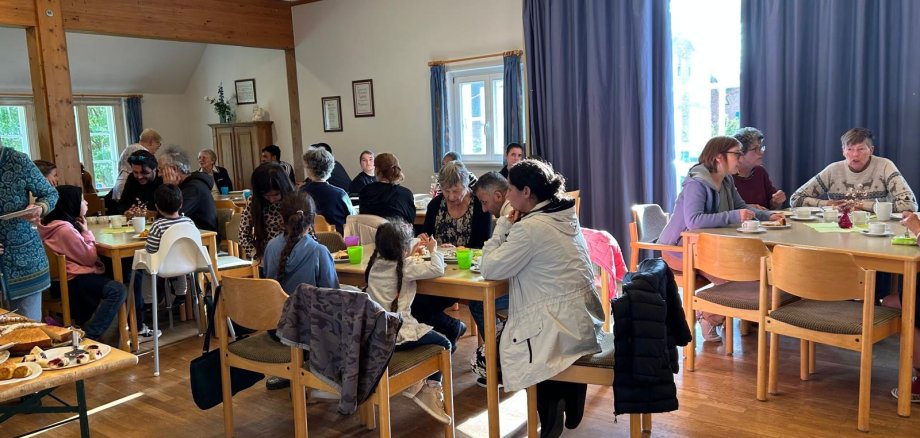 Gäste sitzen in Gruppen an Tischen und unterhalten sich beim gemeinsamen Kaffeetrinken in gemütlicher Atmosphäre.