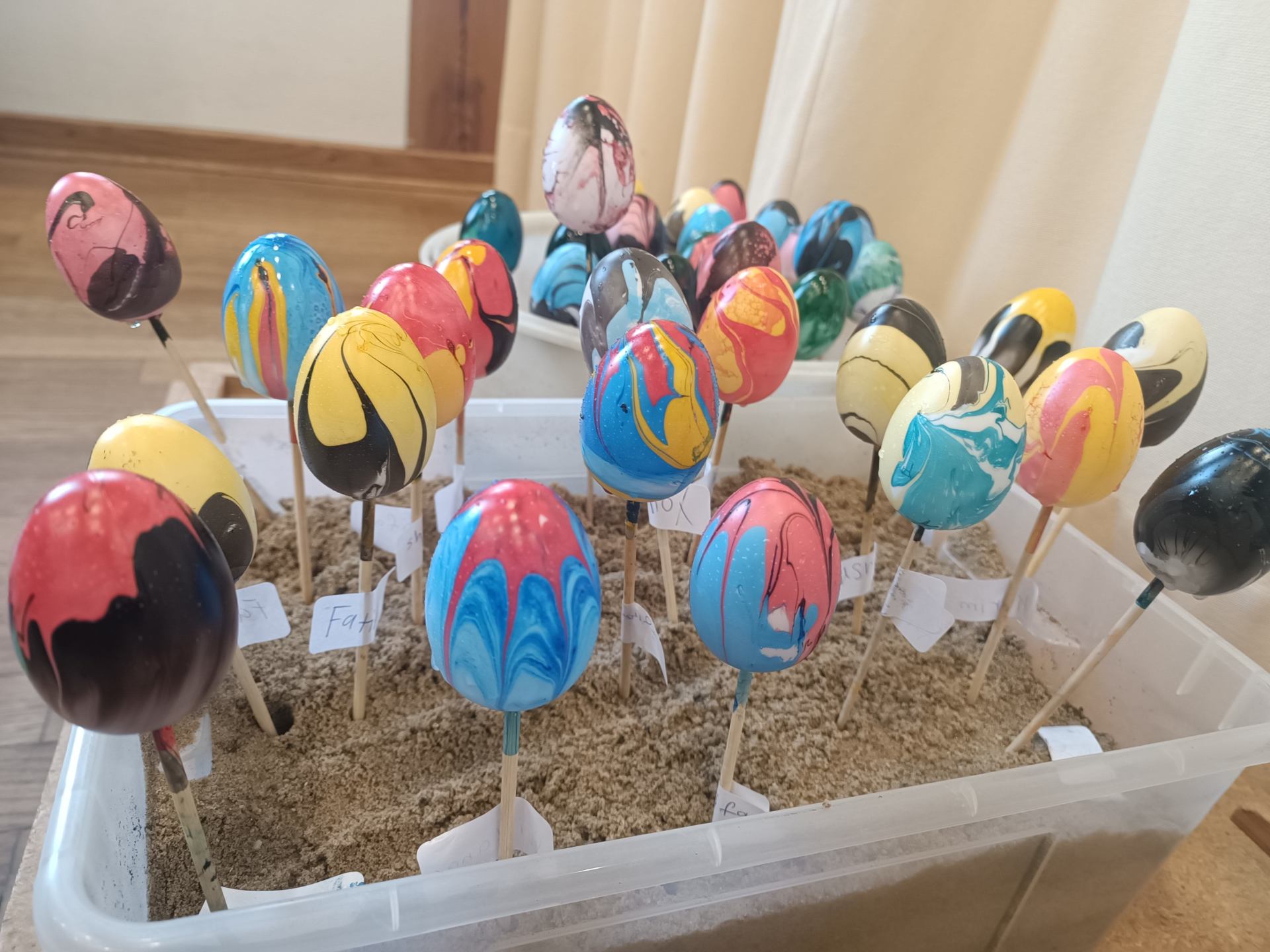 Bunt gefärbte Ostereier mit marmorierten Mustern stecken auf Holzstäbchen in einer Kiste mit Sand zum Trocknen.
