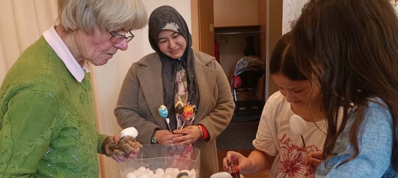 Eine Gruppe aus Erwachsenen und Kindern gestaltet gemeinsam Ostereier an einem Tisch mit verschiedenen Farben und Materialien.