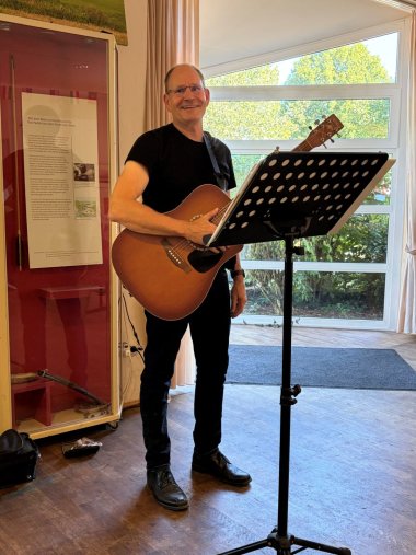 Ein Musiker mit Gitarre steht vor einem Notenständer und sorgt für die musikalische Begleitung der Veranstaltung.