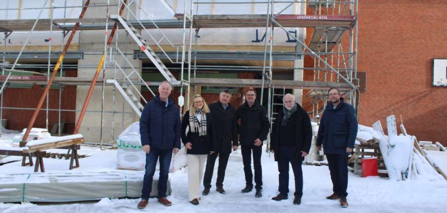Gruppenfoto auf einer verschneiten Baustelle vor einem eingerüsteten Backsteingebäude. Abgebildet sind Amtsvorsteher Ulrich Hardtke, Leitende Verwaltungsbeamtin Tina Knuth, stellvertretender Leitender Verwaltungsbeamter Sebastian Flint, Bürgermeister Rainer Rexin (Sandesneben) sowie die Architekten Fred Freinsheimer und Bernd Müller.