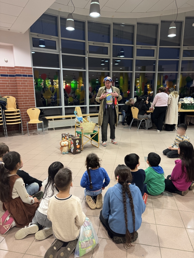 Ein Künstler erzählt Kindern in einer Aula eine Geschichte.