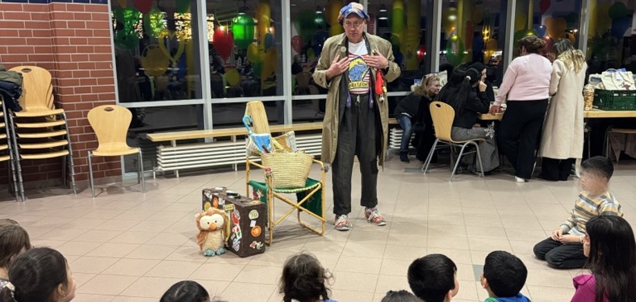 Ein Künstler erzählt Kindern in einer Aula eine Geschichte.
