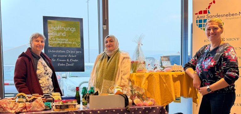 Stand mit selbstgemachten Produkten, drei Frauen posieren davor.