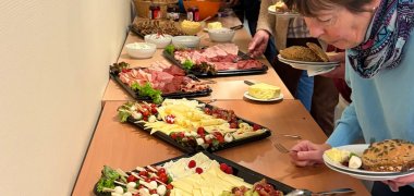 Gäste bedienen sich an einem reichhaltigen Frühstücksbuffet mit Brot, Aufschnitt, Käse, Obst und Gemüse.