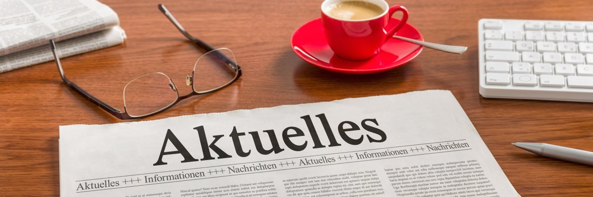 Zeitung auf Schreibtisch - Aktuelles Zeitung mit der Überschrift ‚Aktuelles‘ auf einem Schreibtisch mit Brille, Tastatur und Kaffeetasse.