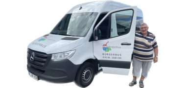 Der weiße Bürgerbus mit Sponsorenaufklebern und geöffneter Fahrertür. Neben der geöffneten Fahrertür steht ein Bürgerbusfaher. Der weiße Bürgerbus mit Sponsorenaufklebern und geöffneter Fahrertür. Neben der geöffneten Fahrertür steht ein Bürgerbusfaher.