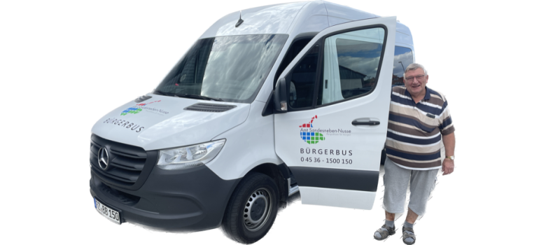 Ein Mann steht neben dem weißen Bürgerbus des Amtes Sandesneben-Nusse mit geöffneter Fahrertür. Auf dem Fahrzeug sind das Amtslogo und die Telefonnummer 04536 - 1500 150 zu sehen.