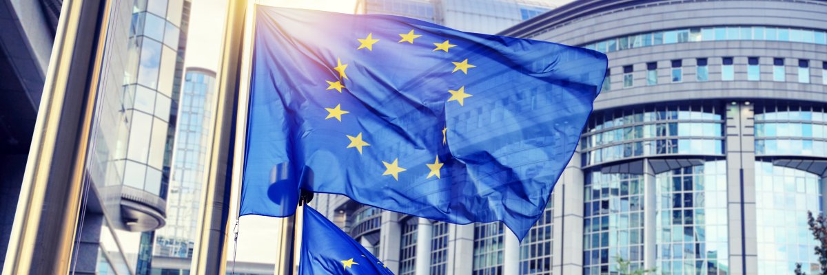 Mehrere wehende EU-Flaggen vor dem Gebäude des Europäischen Parlaments in Brüssel bei Sonnenschein.