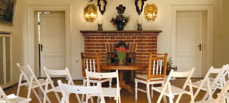 Trauzimmer mit festlich arrangierten Stühlen, Holztisch, Blumenschmuck und Kamin – stimmungsvolle Atmosphäre für standesamtliche Eheschließungen.
